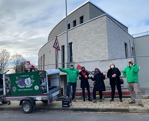 Zwei Mitgleider der Irlandfreunde Leverkusen e.V. und drei Mitarbeiterinnen von PalliLev stehen neben einem grünen Anhänger mit Irlandfreundeaufdruck vor dem Bauzaun von PalliLev. Alle fünf tragen Mund-Nasen-Schutze.