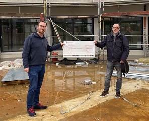 Vor der Baustelle von PalliLev präsentieren zwei Männer einen Karton Wein und eine einzelne Flasche Wein