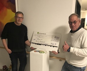Peter Rösgen und ein Handballkollege stehen im Flur des PalliLev-Hospizes mit einem Spendenscheck und vielen Scheinen.